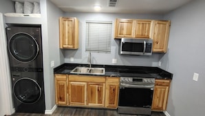 Una cocina compacta con armarios de madera, un lavamanos de acero inoxidable, microondas, lavavajillas y lavadora.