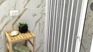 Une salle de bain aux murs recouverts de marbre, une étagère en bois avec des serviettes, une plante en pot et une cabine de douche à rayures.
