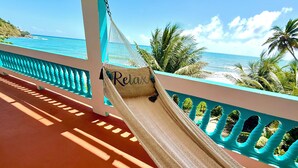 A hammock on a balcony with a view of the ocean and palm trees. - Stay Local at Your Beachfront Casa in Paradise (Maunabo)