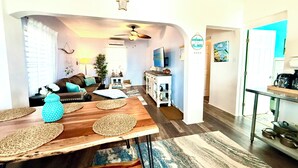 A spacious living area with a wooden dining table, a sofa, and a kitchen in the background. - Stay Local at Your Beachfront Casa in Paradise (Maunabo)