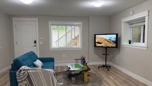 A living room with a blue sofa, a television, a small play area, and a window with a view of a staircase.