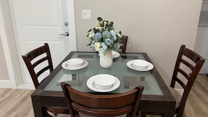 A dining table with four chairs, a vase with flowers, and two light switches on the wall.
