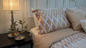 A neatly made bed with patterned pillows, a bedside lamp, and a decorative plant on a nightstand.