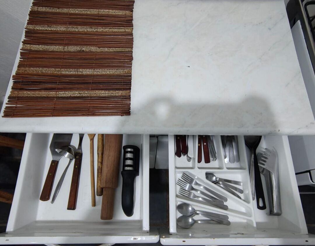A drawer with various kitchen utensils including knives, spoons, and a rolling pin.
