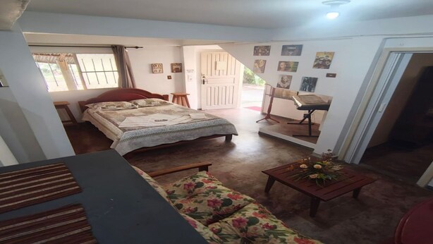 A bedroom with a bed, a floral sofa, a small table with flowers, a desk with a chair, and a door leading to another room.