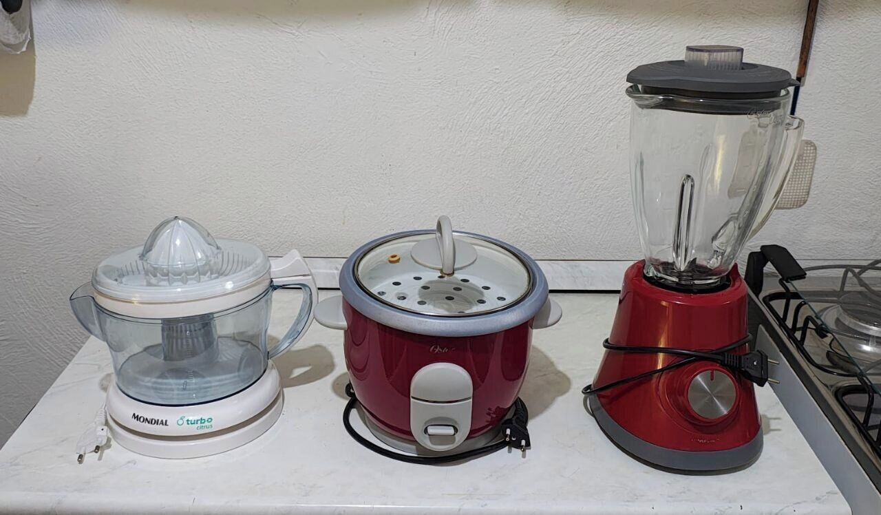 Três eletrodomésticos de cozinha: um liquidificador, um processador de alimentos e um centrífuga, sobre uma bancada.