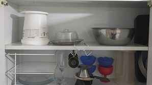 A kitchen with a coffee maker, a kettle, a pot, a bowl, and a shelf with glassware.