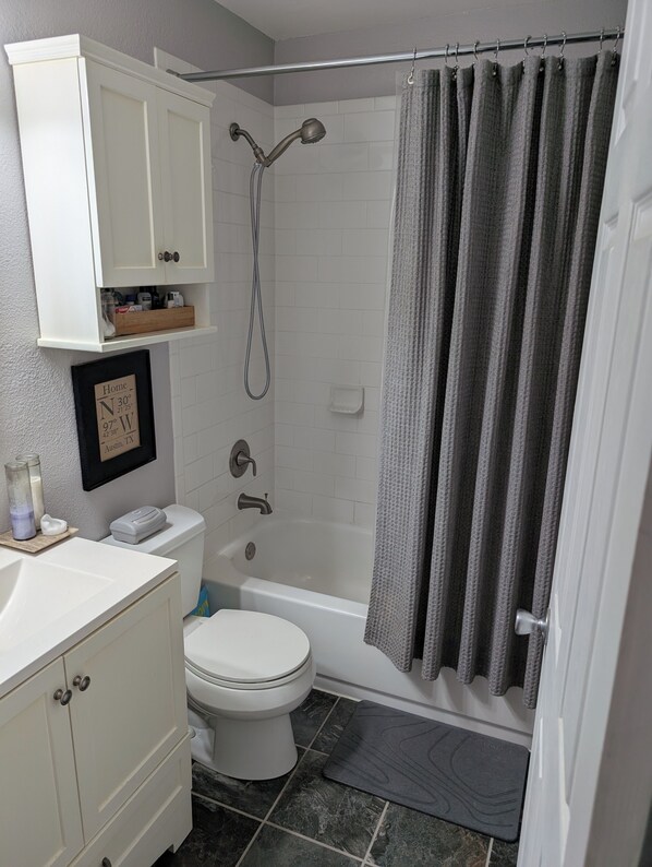 Une salle de bain comprenant des toilettes, un lavabo, un meuble de rangement, une douche et un panneau encadré accroché au mur.