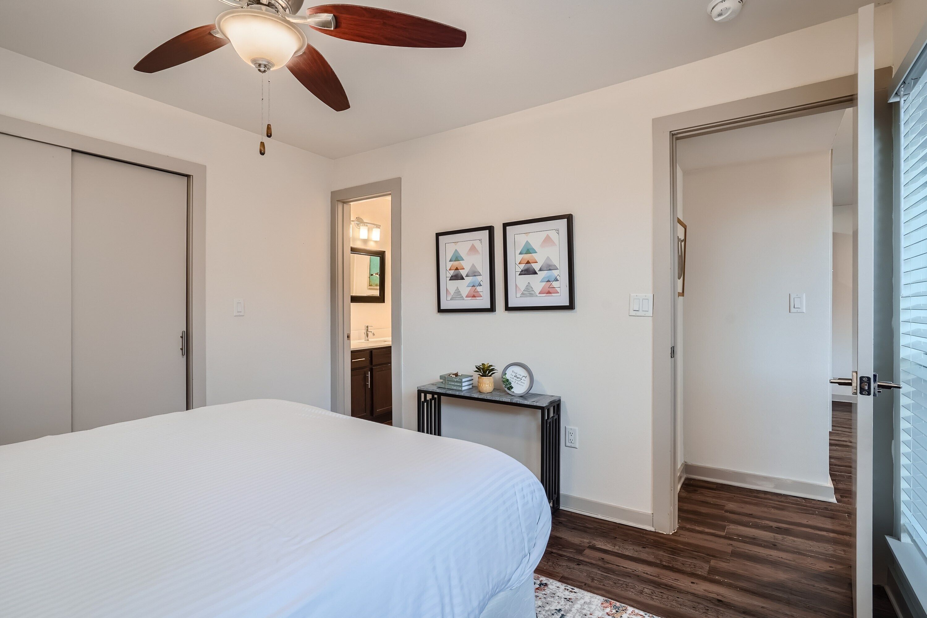 Un dormitorio con cama, ventilador de techo, mesita de noche y puerta que da a otra habitación.