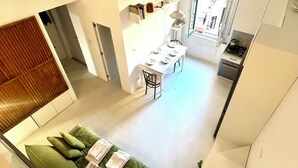 A modern interior with a dining area, kitchen, and a green sofa with cushions.