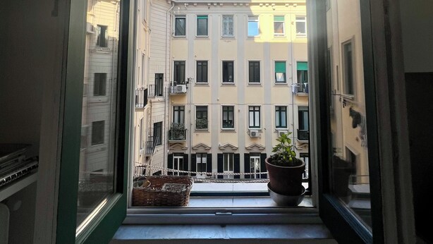A view from a balcony with a clear blue sky, a potted plant, and a building with multiple windows and balconies.