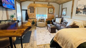 A cozy cabin interior with a wooden ceiling, a TV, a sofa, a coffee table, and a bed.
