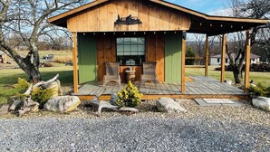 A wooden cabin with a porch, two wicker chairs, a welcome sign, and a gravel driveway.