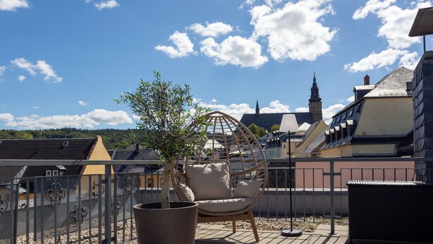 En takterrass med en hängstol, en krukväxt och utsikt över ett kyrktorn.
