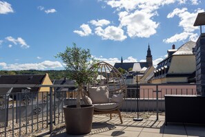 A rooftop terrace with a hanging chair, a potted plant, and a view of a church tower.