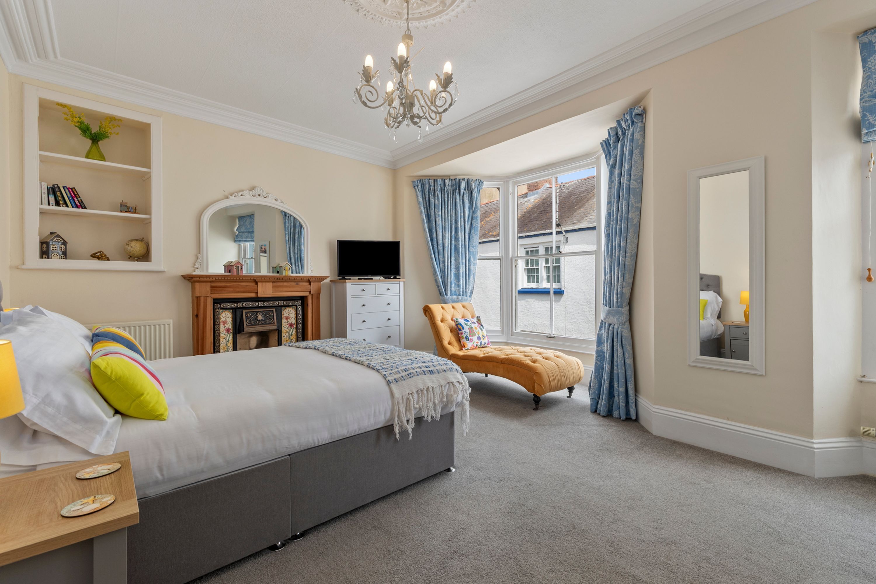 A bedroom with a bed, a television, a chair, a dresser, and a window with curtains.