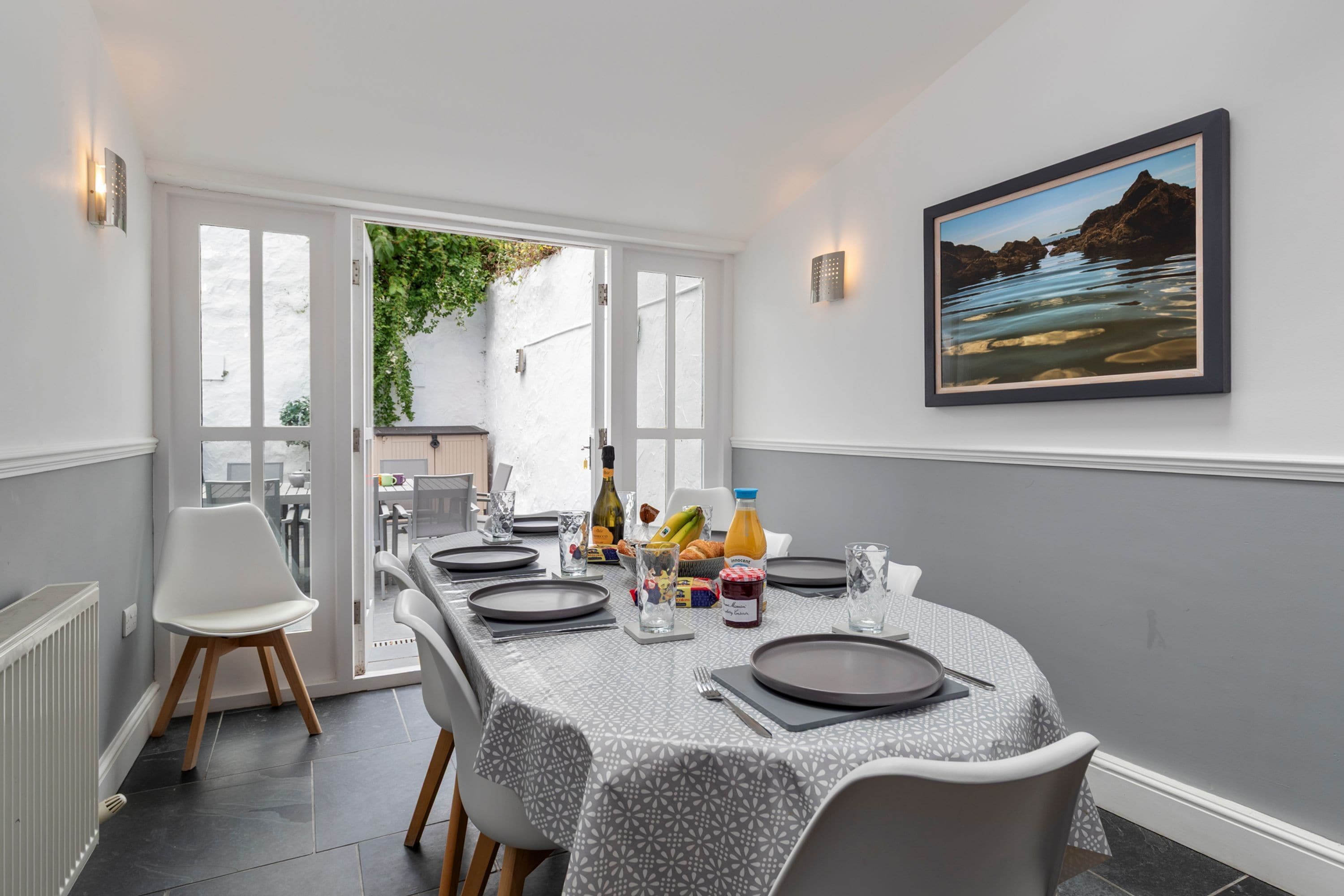 Un coin repas avec une table dressée pour quatre personnes, une bouteille de vin et un panier de fruits.