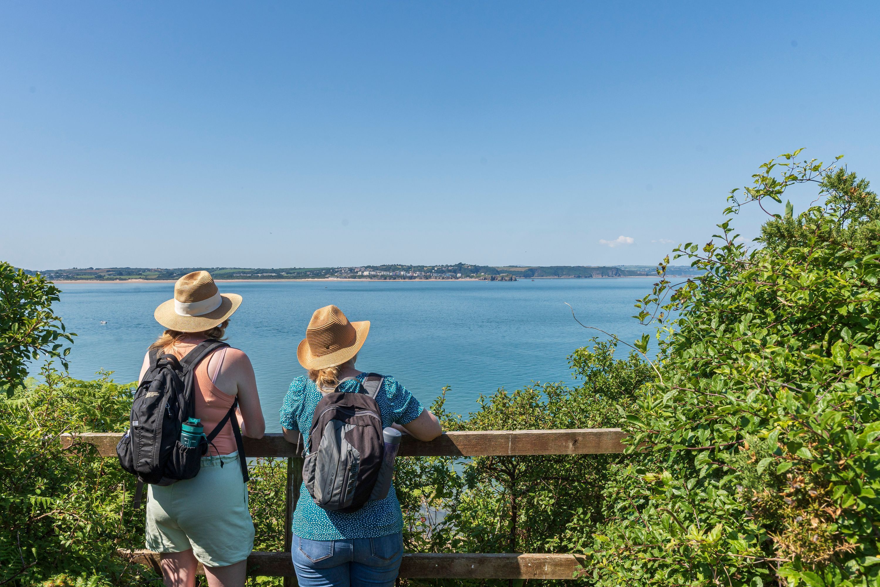 Two people standing by a wooden railing overlooking a body of water with a distant shoreline.