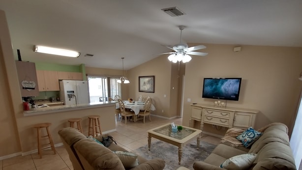 A living room with a sofa, a coffee table, and a TV. There is a kitchen area with a refrigerator and a dining table.
