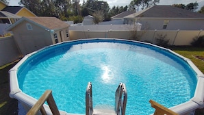 An above-ground swimming pool with a wooden deck and ladder.