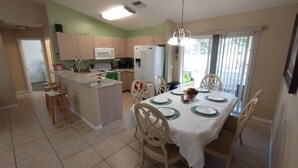 A modern kitchen with a dining area, featuring a central island, wooden chairs, and a table set for four.