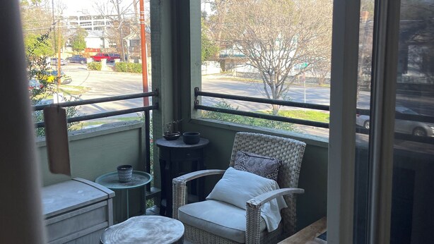 A balcony with wicker furniture, a ceiling fan, and a view of a parking lot and trees.