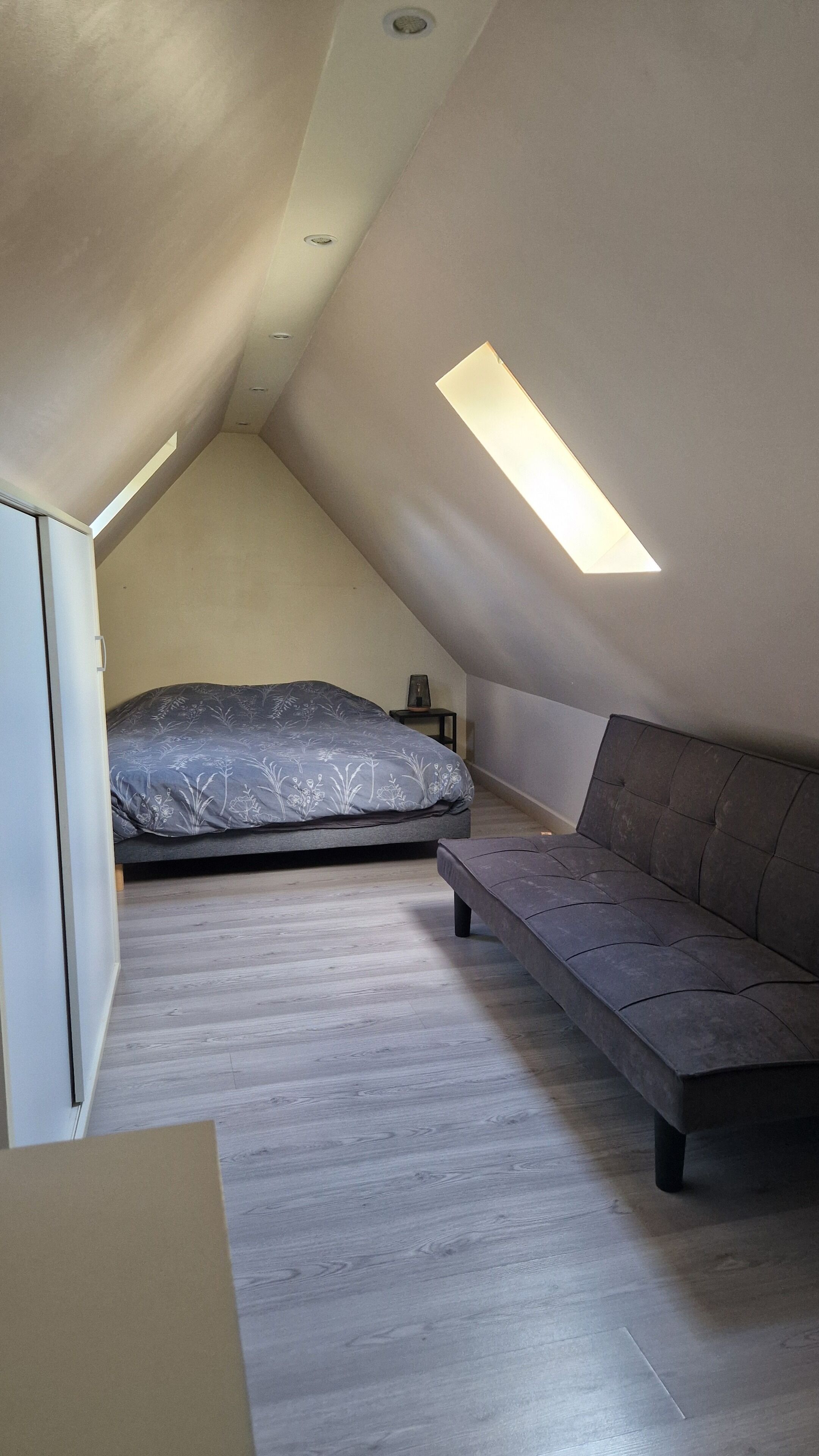 A small attic bedroom with a sloped ceiling, a bed, a sofa, and a skylight.