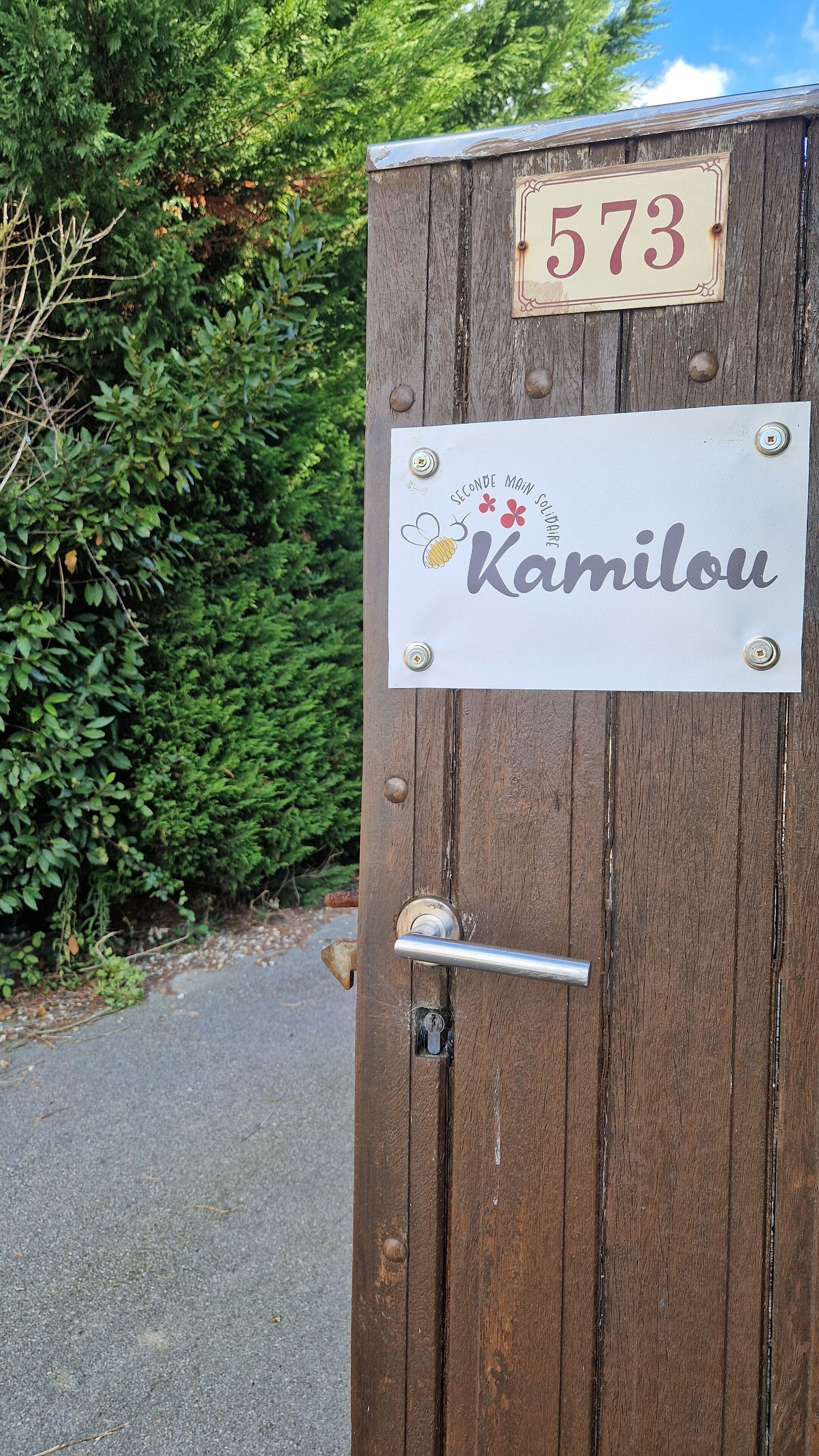 Une porte en bois avec une plaque portant l’inscription « 573 Kamilou » et une serrure.