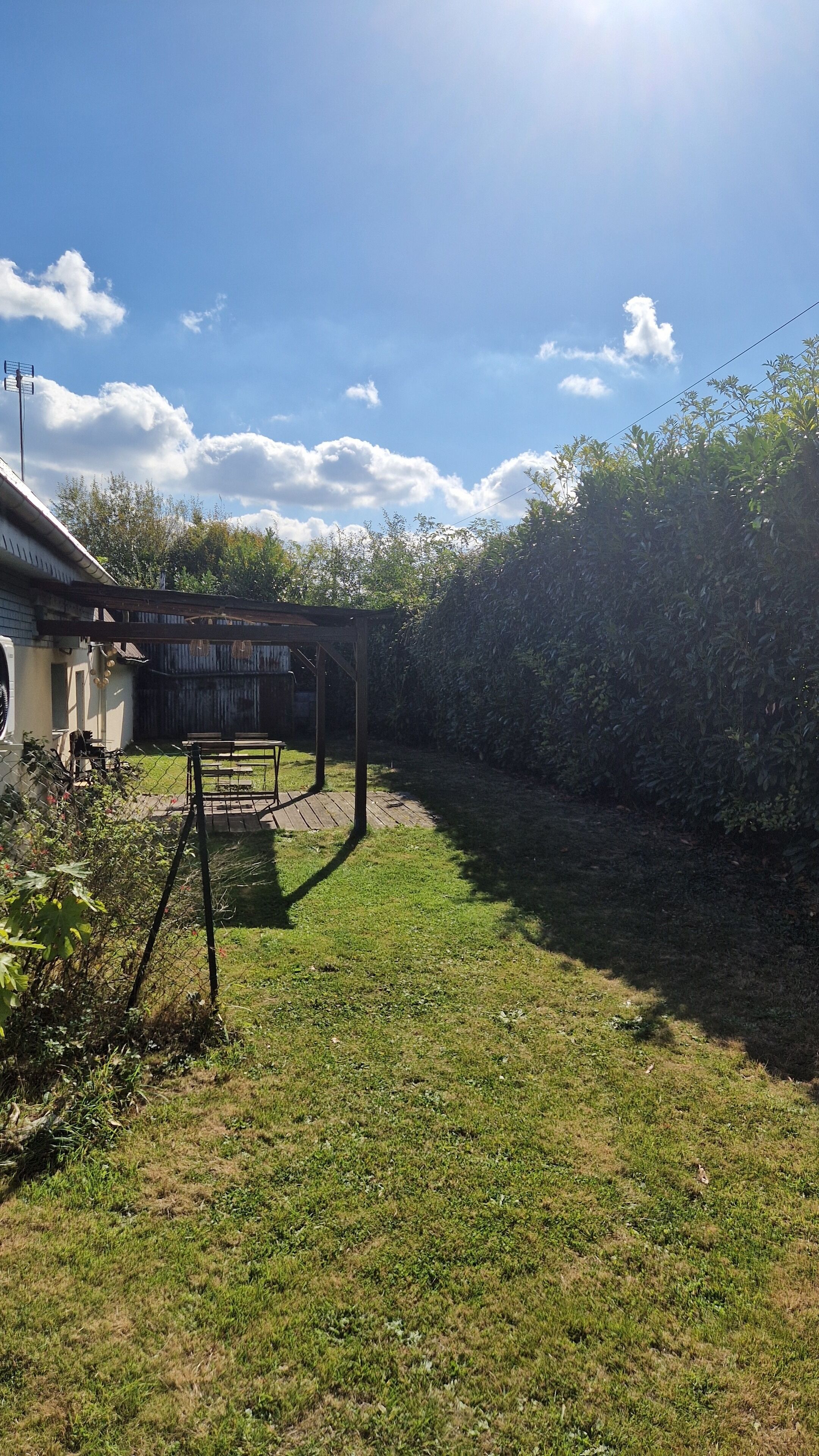 A backyard with a wooden deck, a pergola, and a fenced area.