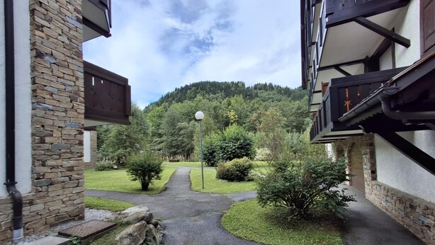 A courtyard with a stone wall, a pathway leading to a gate, and a view of a forested hill.