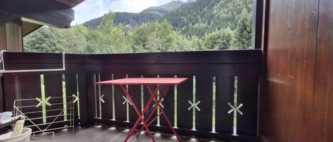 A balcony with a red table and metal rack, overlooking a forested mountain.