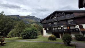 A multi-story building with balconies, surrounded by lush greenery and mountains in the background.