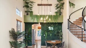 Un vaste espace dédié à la salle à manger, avec une table ronde en bois et des chaises, entouré d’une végétation luxuriante et agrémenté d’un plafond en bois.