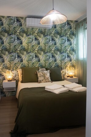 Camera da letto con un letto grande, due comodini con lampade, una ventola a soffitto e carta da parati con motivo a foglia tropicale.
