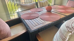 A balcony with a table set for dining, wicker chairs, and a view of buildings in the background.