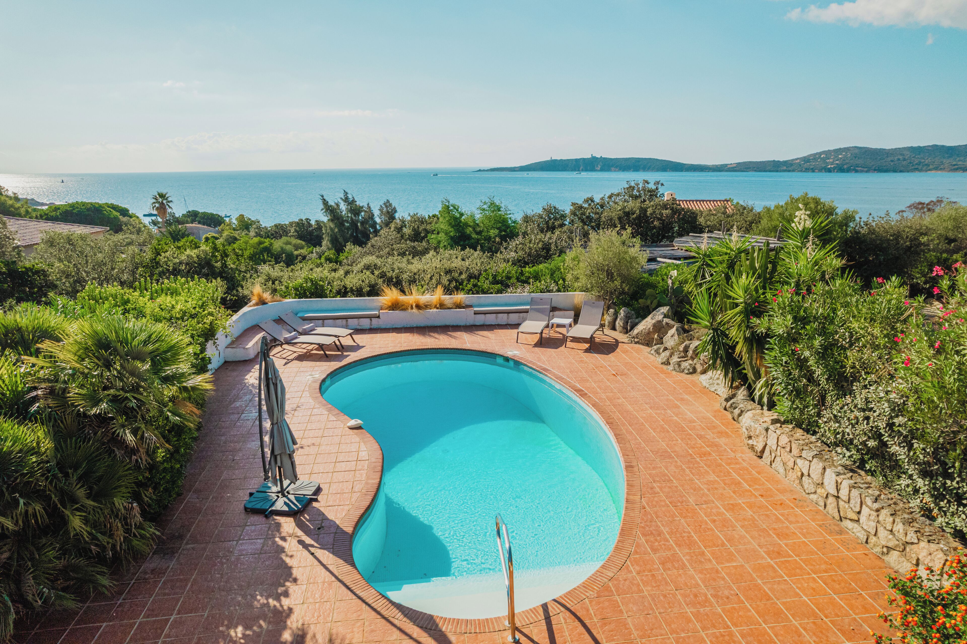A swimming pool with a curved edge, surrounded by a stone wall and lush greenery.