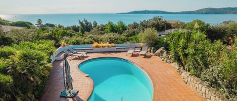 A swimming pool with a curved edge, surrounded by a stone wall and lush greenery.