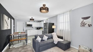 A modern living room with a grey sofa, a dining table, and a kitchen in the background. - Modern Guesthouse with W/D, 6 mins to DT St Pete (St. Petersburg)
