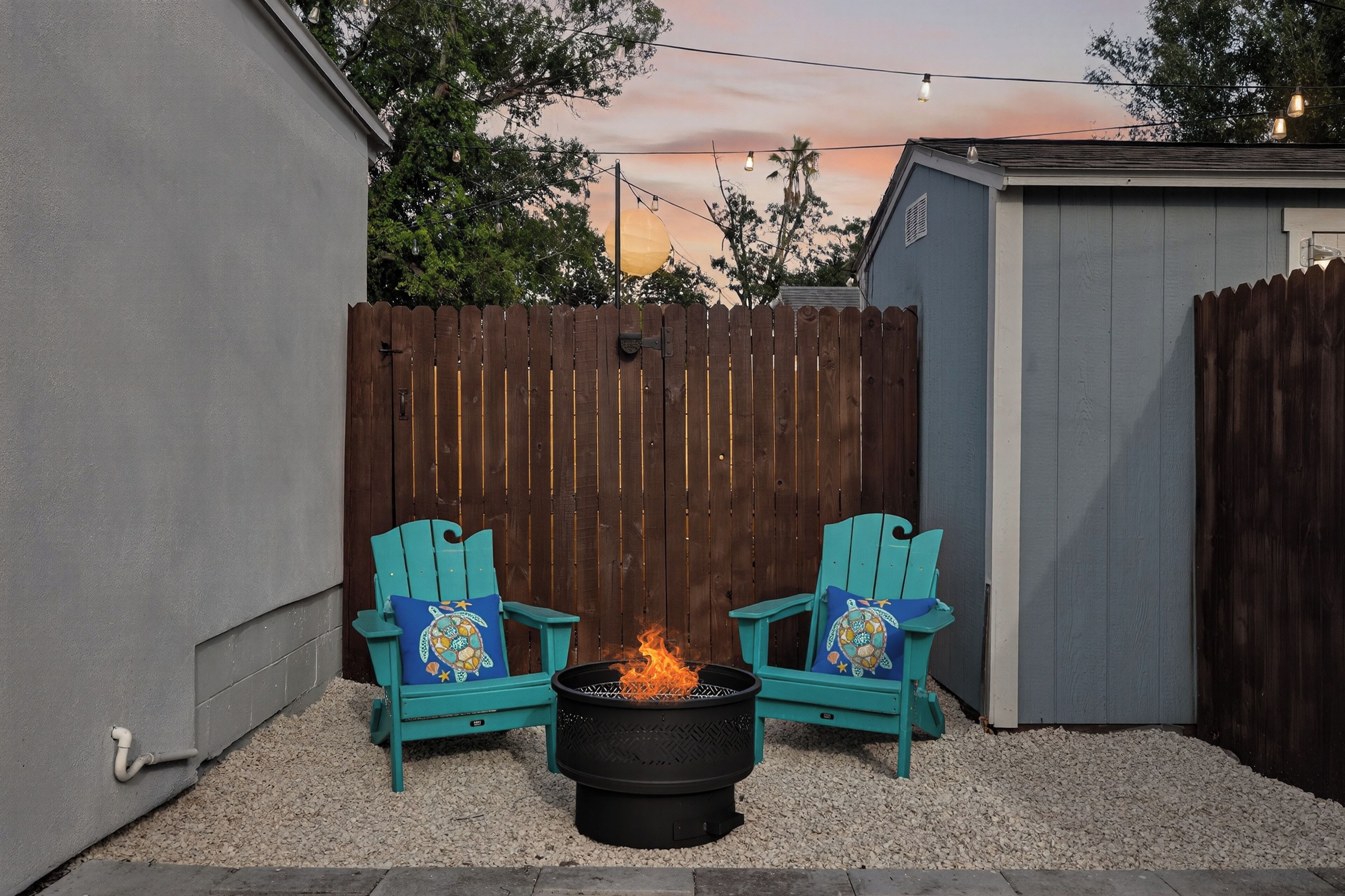 A backyard with a fire pit and two turquoise Adirondack chairs with decorative pillows.