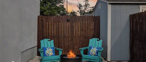 A backyard with a fire pit and two turquoise Adirondack chairs with decorative pillows.