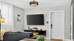 A modern living room with a grey sofa, a flat-screen TV mounted on the wall, a fireplace, and a white door. - Modern Guesthouse with W/D, 6 mins to DT St Pete (St. Petersburg)