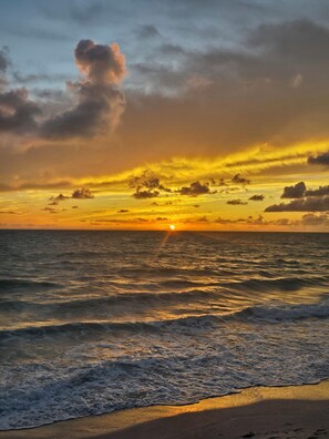 Um pôr do sol sobre o oceano, com ondas chegando à praia.