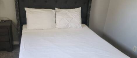 Una cama bien hecha con un cabecero oscuro y dos almohadas.