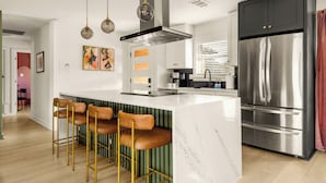 Una cocina moderna con refrigerador de acero inoxidable, una isla de mármol y taburetes de bar.