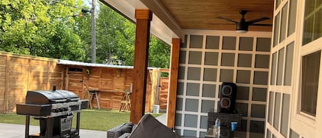 A covered patio with a grill, seating, and a ceiling fan.
