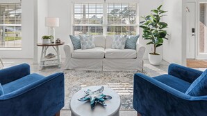 Ein Wohnzimmer mit einem weißen Sofa, blauen Sessel, einem Couchtisch und einer Topfpflanze.