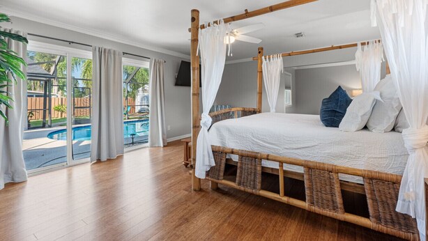 Ein geräumiges Schlafzimmer mit Himmelbett, großem Fenster und Blick auf ein Außenbecken.