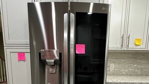 Ein Edelstahl-Kühlschrank mit Wasserspender in einer Küche mit grauen Schränken und Marmorböden.