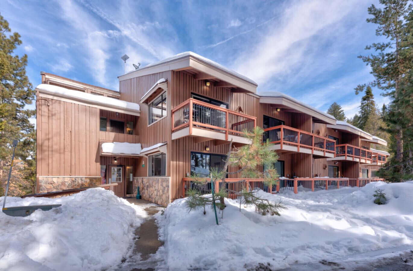A multi-story wooden building with balconies, a stone foundation, and a snowy landscape.
