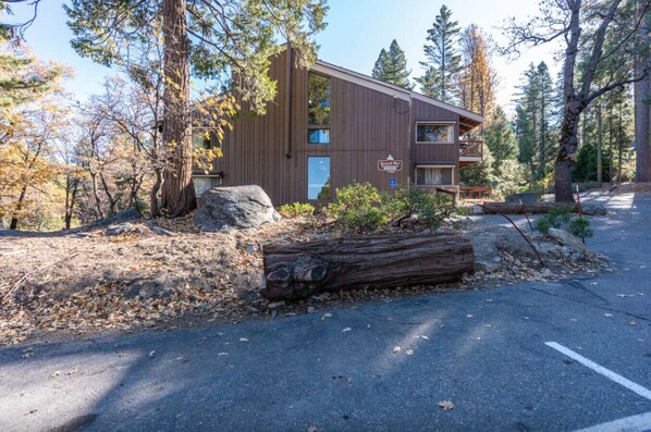 Une cabane avec une façade en bois, un gros rocher devant et une bûche sur l’allée.